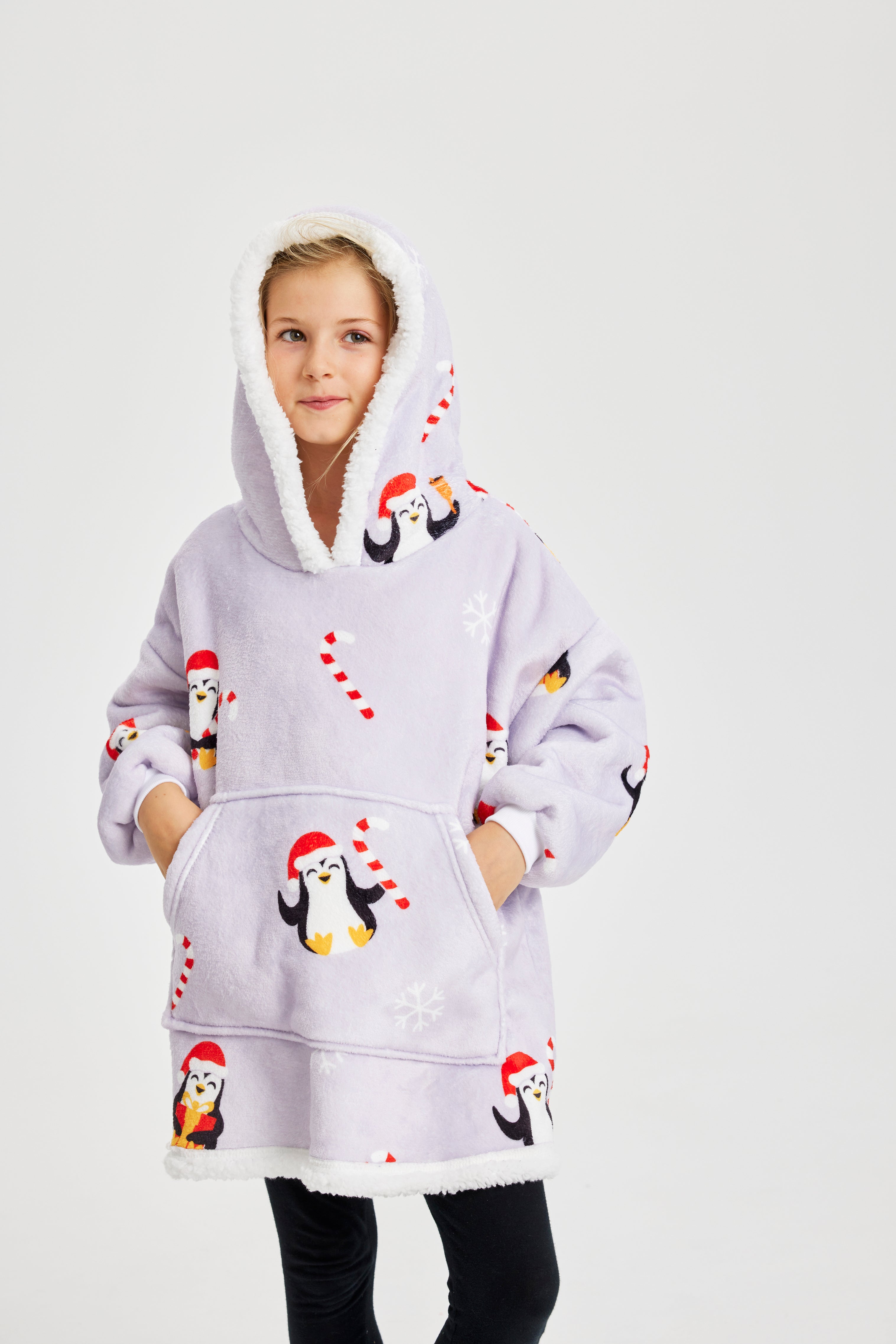 Un enfant, les mains dans les poches, vêtu d'un sweat à capuche de Noël violet clair avec des pingouins dessus.